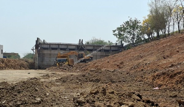 Heavy yellow excavators working near a massive concrete retaining structure at the Prestige Kollur site in Kollur, Hyderabad