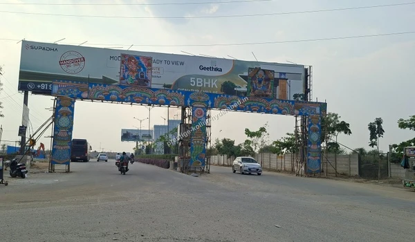 A large decorative grand entrance archway over a wide road with billboards, illustrating the developing infrastructure of the Kollur location in Hyderabad.